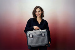 Woman holding a silver suitcase against a gradient background