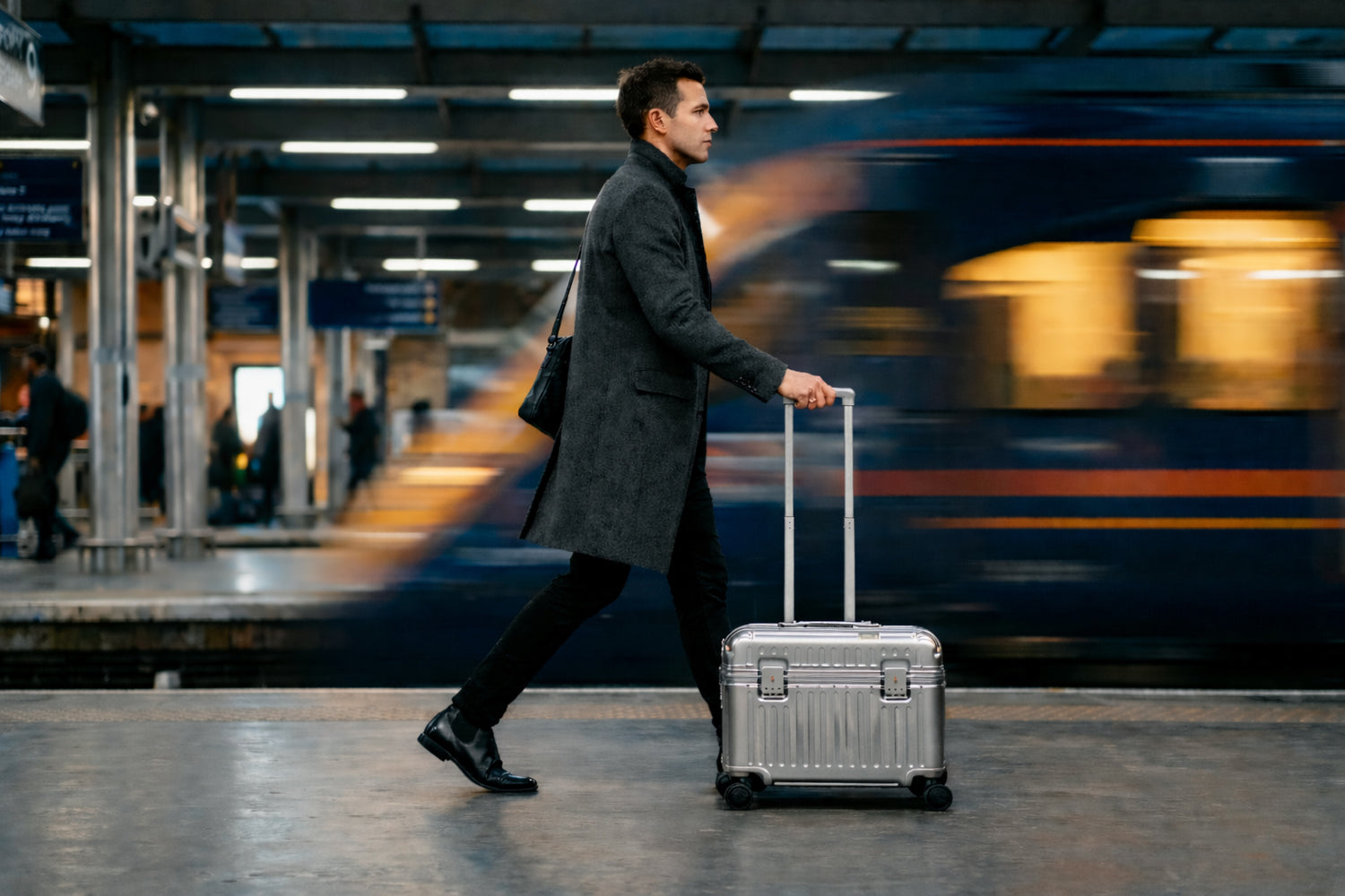 Man with a Portar Top Open polycarbonate shell with aluminum edgeframe suitcase walking on a train platform with a blurred train in the background