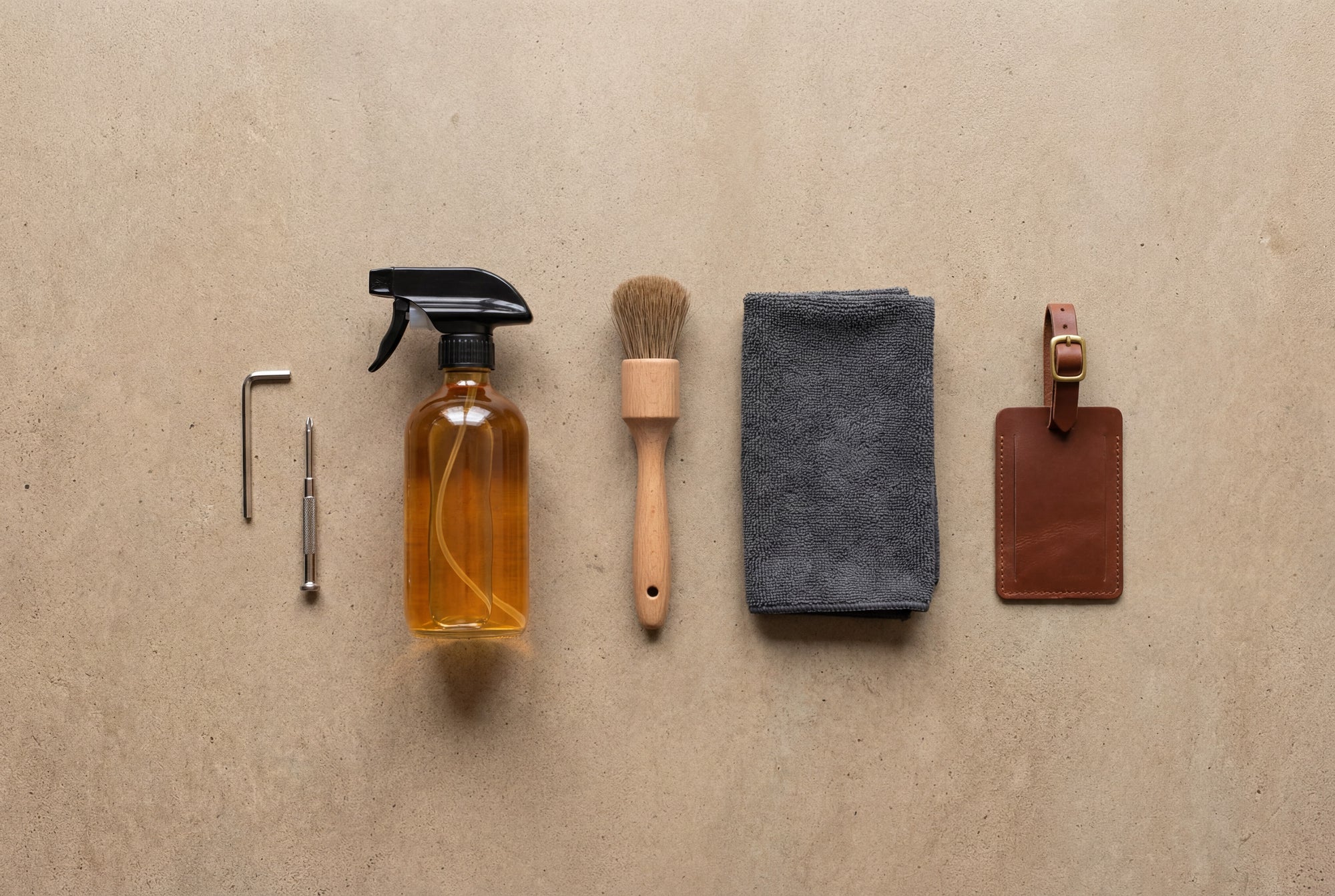Set of leather care products including a spray bottle, brush, cloth, and tag on a beige background