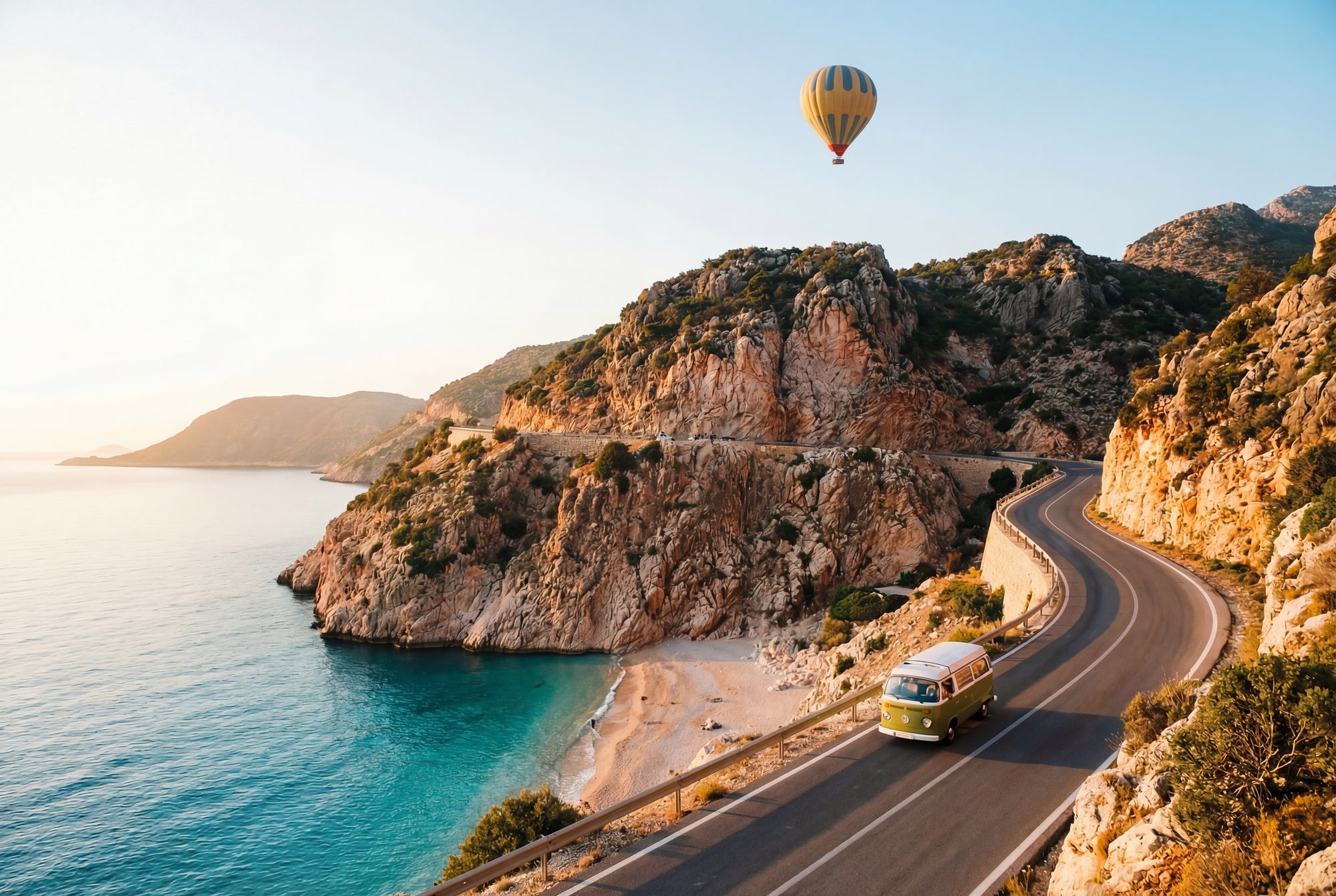 Van driving along a coastal road with a hot air balloon in the sky.