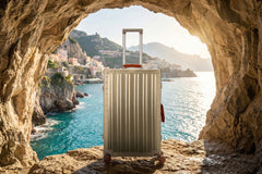 Portar Gold Aluminum Suitcase placed in a natural stone archway with a scenic view of a coastal town.