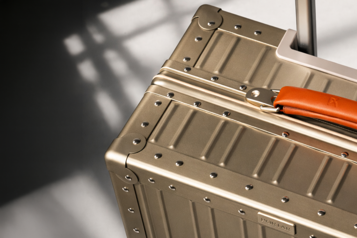 Lucent Gold suitcase with orange handle on a gray background