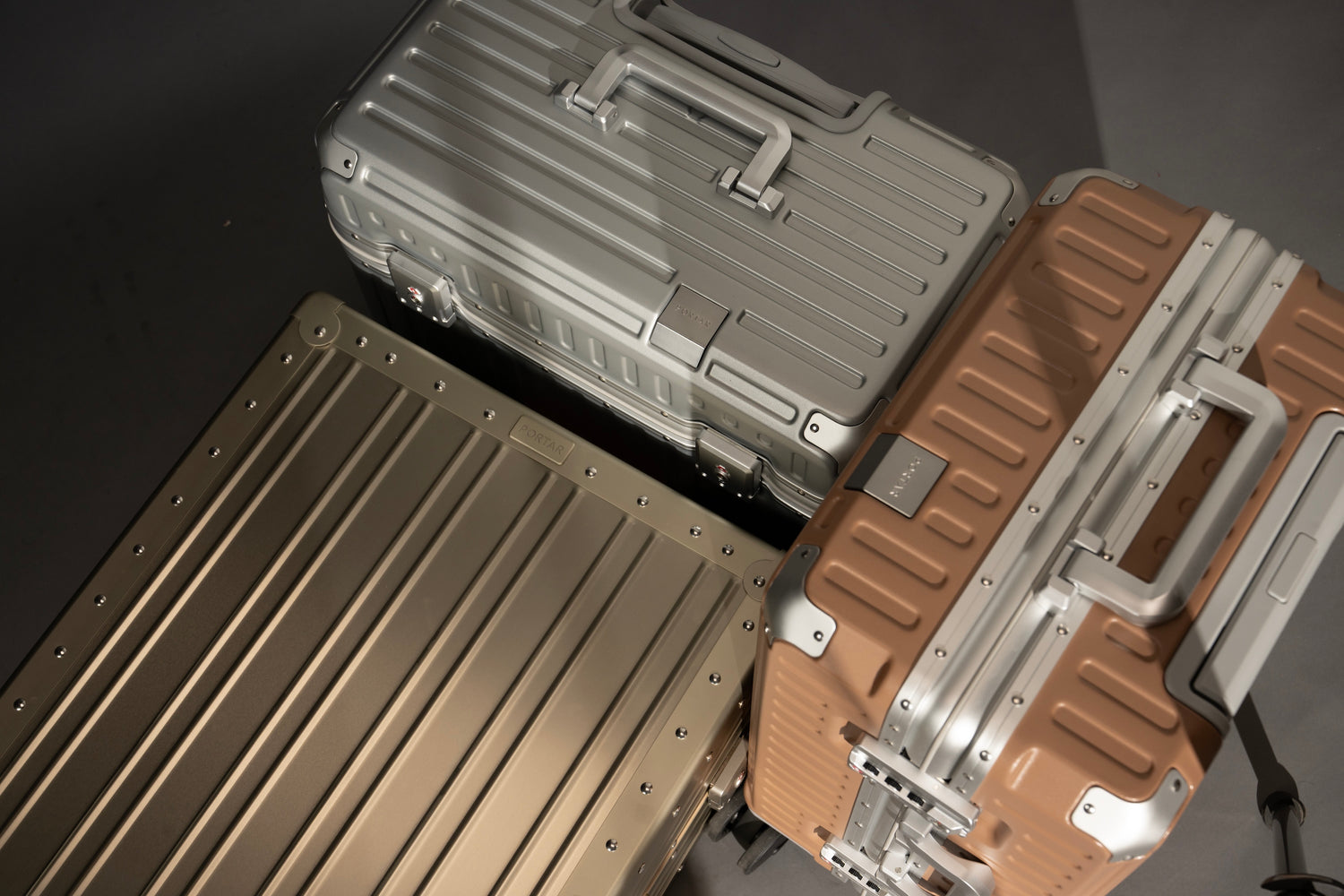 Three Portar suitcases in different colors on a reflective surface.