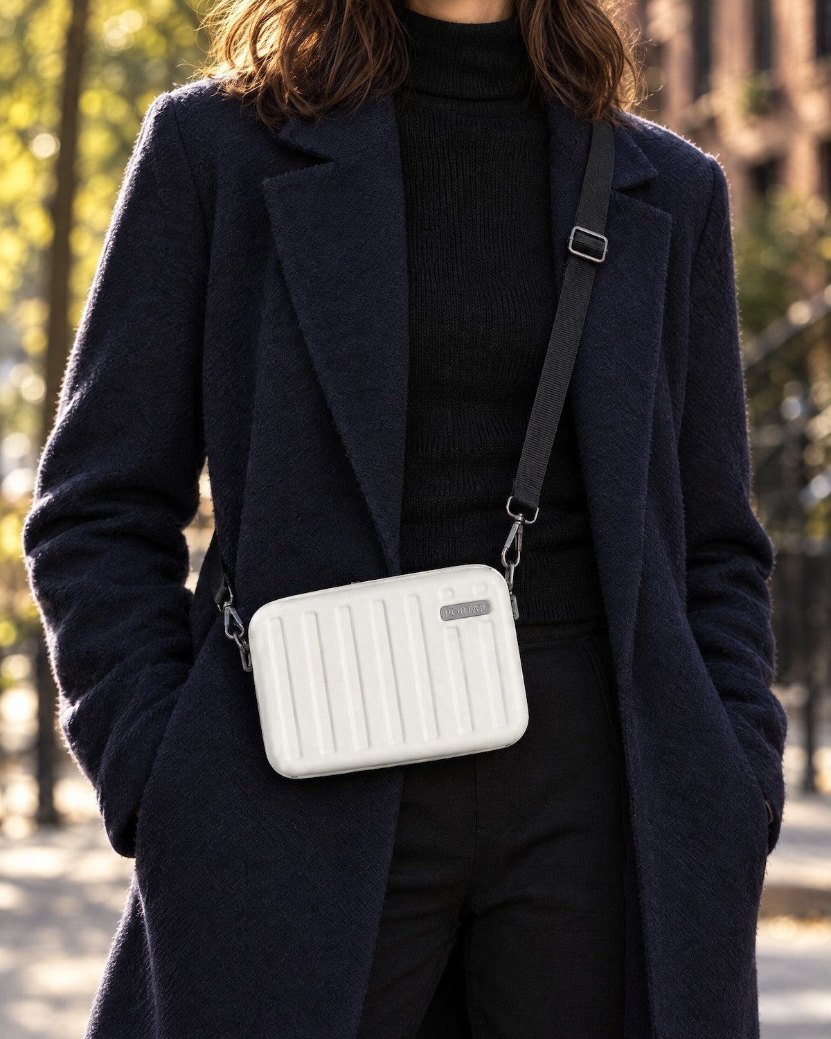 Woman wearing the Portar Solace crossbody bag in Cloud Dancer White over a navy coat on a city street