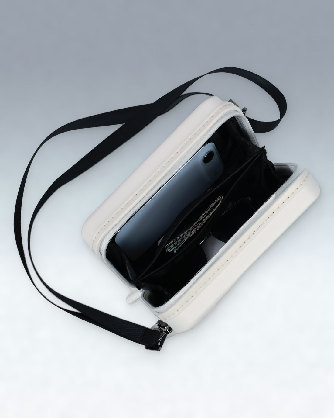 A white zippered Portar crossbody bag with a black shoulder strap, shown open with a smartphone and pen inside, on a light gray background.